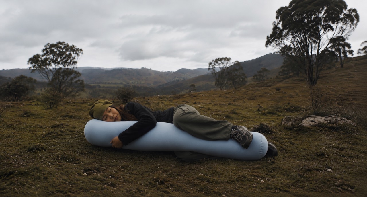 A person resting outdoors while hugging a powder-blue Om pillow